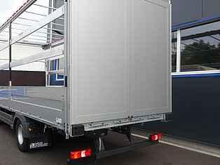 Rückansicht eines offenen LKW-Anhängers nahe einem Gebäude.