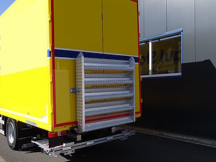 Gelber LKW an einem Ladebereich mit Gebäude.