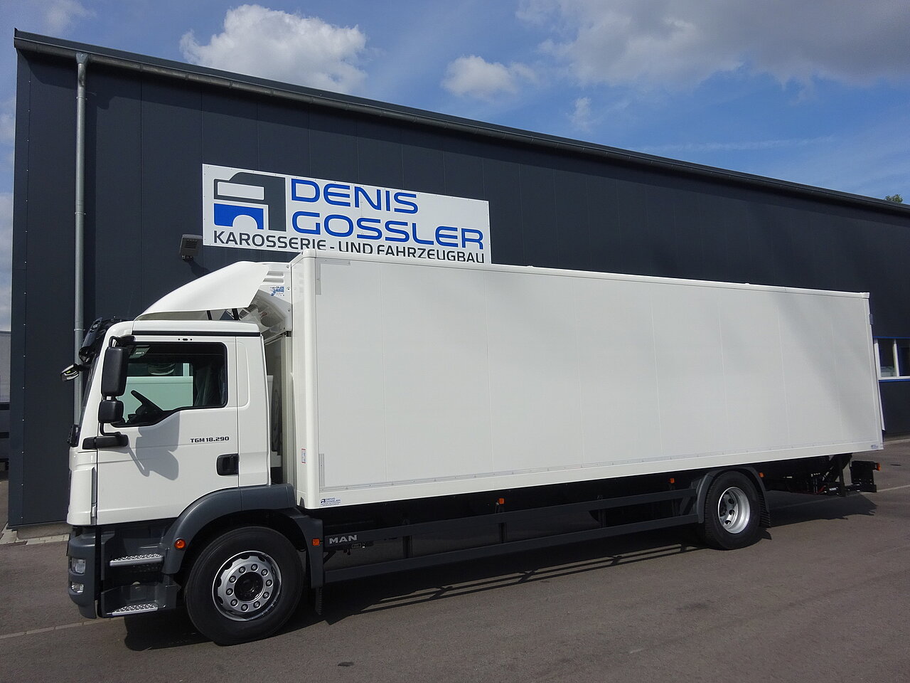 Weißer LKW neben einem Gebäude mit Beschilderung geparkt.