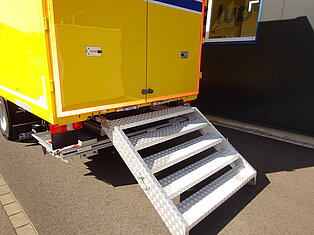 Gelber LKW mit Metallstufen zum Heck.