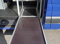 Ein blauer Transporter mit ausgefahrener Laderampe auf Asphalt.