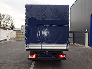 Rückansicht eines LKW mit blauer Plane auf Parkplatz.