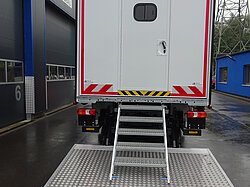 Lkw mit Hecktür und Treppe an einer Anlage.