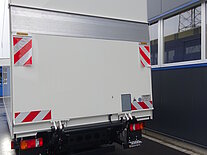Rückansicht eines LKWs mit Palfinger-Lift an einem Gebäude.