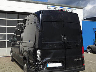 Schwarzer Lieferwagen mit Heckschaden vor Werkstatt