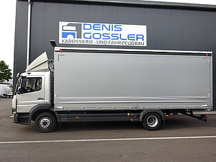Silberner LKW vor einer Werkstatt mit Schild