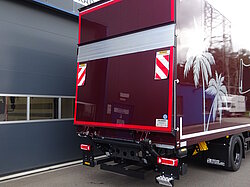 Roter LKW mit Palmenmotiv vor einem Gebäude.