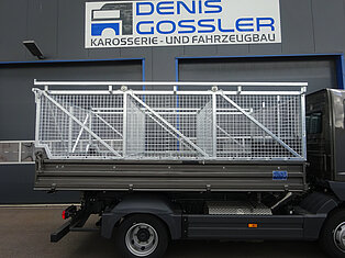 LKW mit Metallkäfig vor einer Werkstatt geparkt.