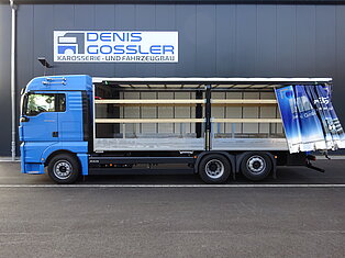 Blauer LKW mit offener Seite vor einem Gebäude geparkt.