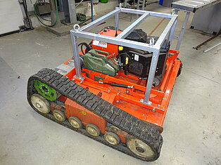 Eine rote Raupenmaschine mit Metallrahmen in einer Werkstatt.