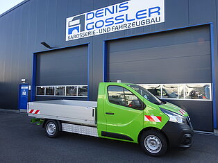 Grüner LKW vor einer Werkstatt mit Beschilderung geparkt.