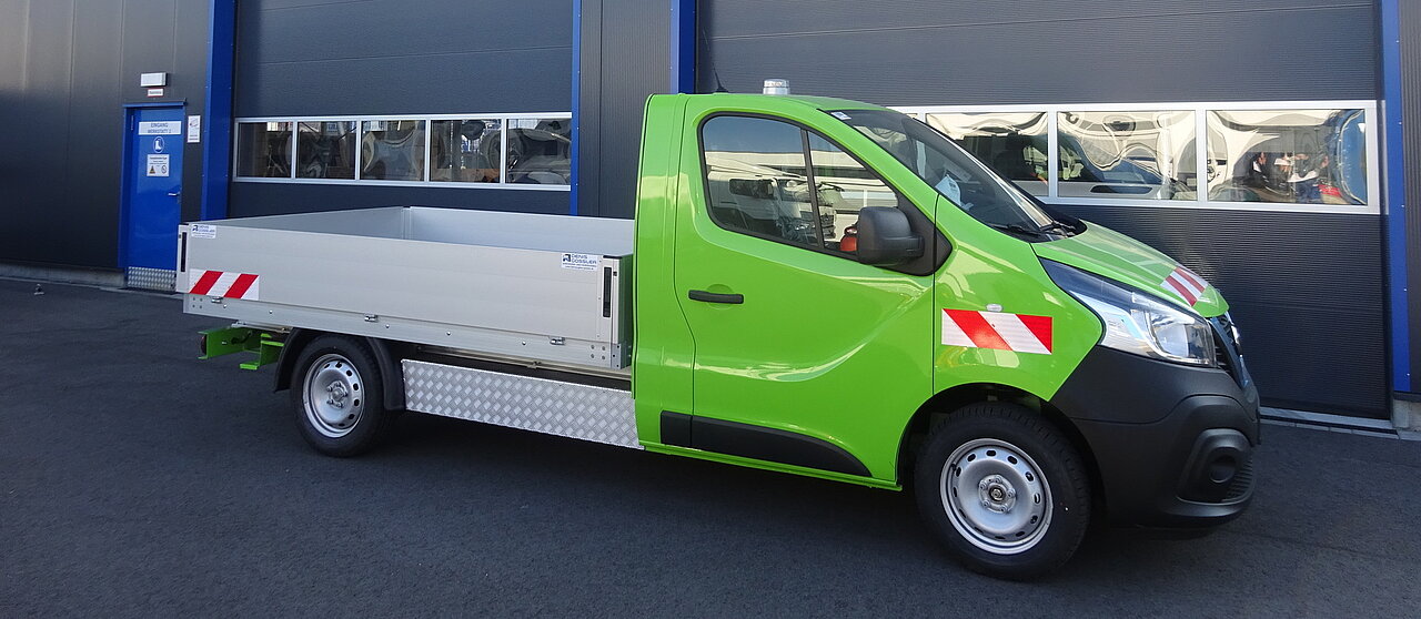 Grüner LKW vor einer Werkstatt mit Beschilderung geparkt.