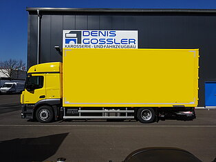 Gelber LKW vor einem Fabrikgebäude geparkt.