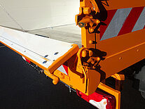 Nahaufnahme einer orangefarbenen LKW-Heckklappe mit roten Streifen.