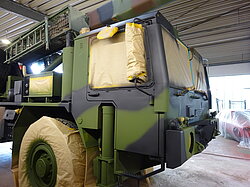 Getarntes Militärfahrzeug in einer Werkstatt, teilweise abgedeckt zum Lackieren.