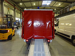 Roter LKW mit Rampe im Lager, Gabelstapler in der Nähe.