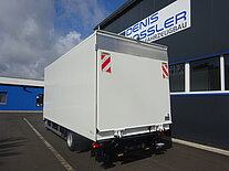 Weißer LKW parkt neben einem blauen und grauen Gebäude.