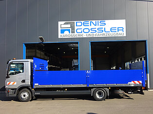Ein blauer LKW steht vor einer Werkstatt mit dem Schild 'Denis Gossler Karosserie- und Fahrzeugbau'.
