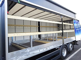 Offener LKW-Anhänger mit Holzträgern innen.