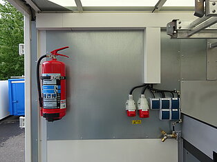 Roter Feuerlöscher und Schalttafel an der Wand.
