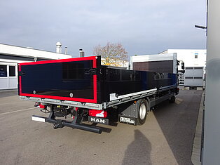 Ein LKW steht auf einem Parkplatz vor einem Gebäude.