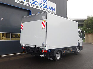 Ein weißer LKW steht vor einer Werkstatt mit dem Schild 'Denis Gossler Karosserie- und Fahrzeugbau'.