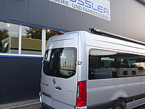 Silberner Transporter vor einer Werkstatt mit Schild