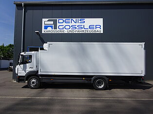 Weißer LKW neben einem Gebäude mit einem Schild.