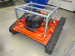Ein Rasenmäher mit Kettenantrieb und Metallrahmen auf Werkstattboden.